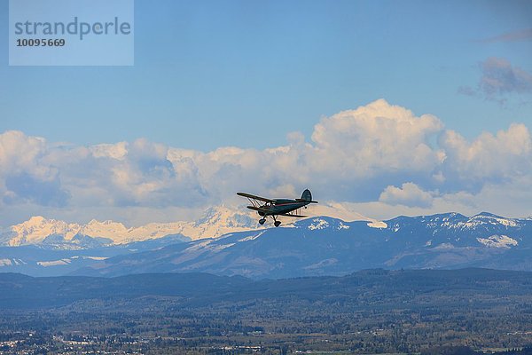 Silhouettiertes Doppeldeckerflugzeug über schneebedeckter Berglandschaft