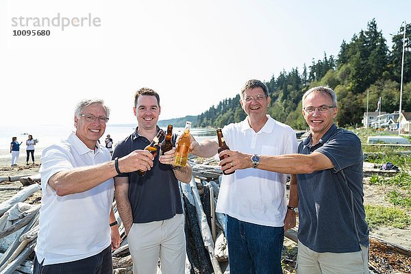 Porträt von reifen Männern und Sohn  die sich mit Flaschenbier am Strand anstoßen.