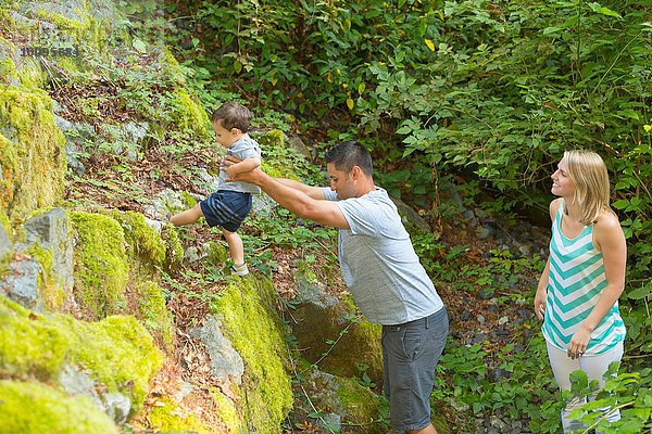 Junger Mann hebt Kleinkind-Sohn auf Steine im Park