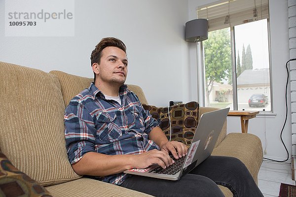 Junger Mann auf dem Sofa sitzend mit Laptop