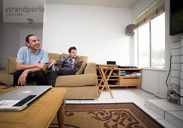 Zwei junge Männer sitzen auf dem Sofa und schauen fern.