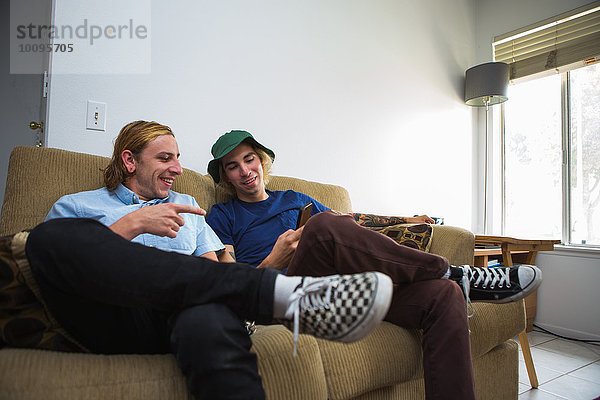 Zwei junge Männer sitzen auf dem Sofa und schauen auf das Smartphone.