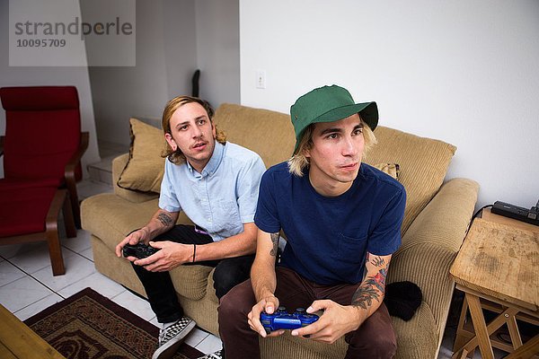 Zwei junge Männer sitzen auf dem Sofa und spielen ein Videospiel.