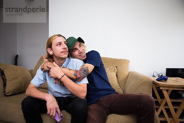 Zwei junge Männer sitzen auf dem Sofa und umarmen sich.
