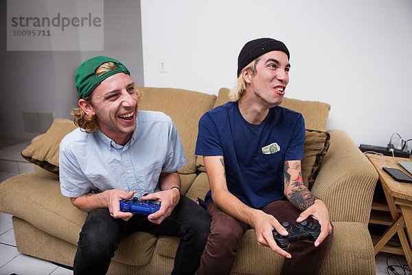 Zwei junge Männer sitzen auf dem Sofa und spielen ein Videospiel.