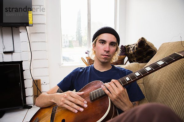 Junger Mann sitzt auf dem Sofa und spielt Gitarre.
