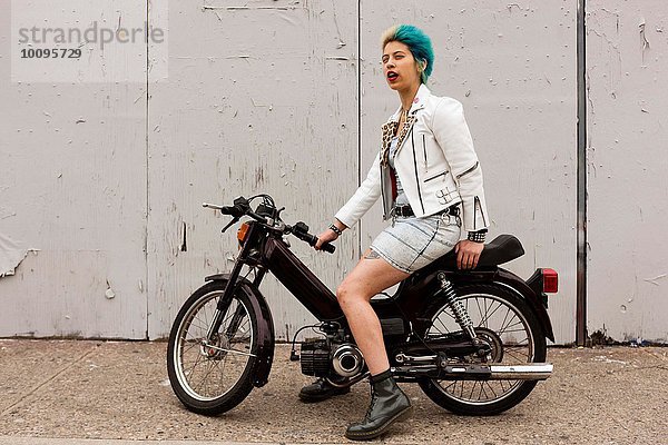 Porträt einer jungen Frau mit bunten Haaren  sitzend auf dem Motorrad