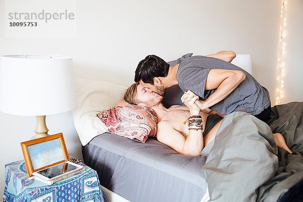 Männliches Paar auf dem Bett  Händchen haltend  küssend