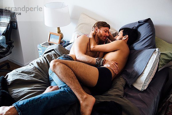 Männliches Paar  teilweise bekleidet  auf dem Bett liegend  umarmend