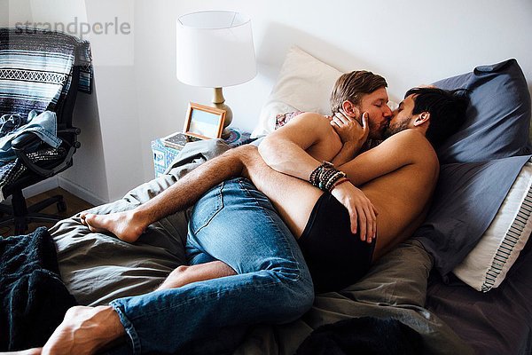 Männliches Paar  teilweise bekleidet  auf dem Bett liegend  küssend