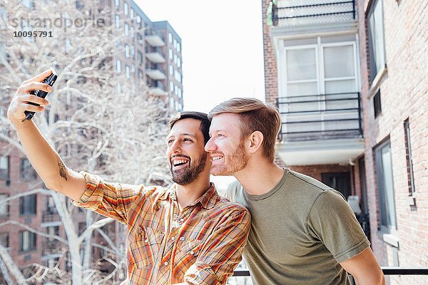 Männliches Paar  das auf dem Balkon steht und sich selbst porträtiert  mit dem Smartphone