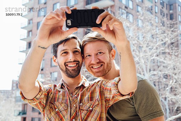 Männliches Paar  das auf dem Balkon steht und sich selbst porträtiert  mit dem Smartphone