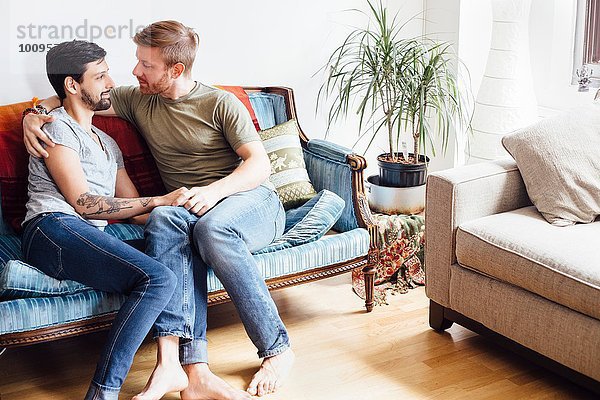 Männliches Paar auf Sofa sitzend  umarmend  von Angesicht zu Angesicht
