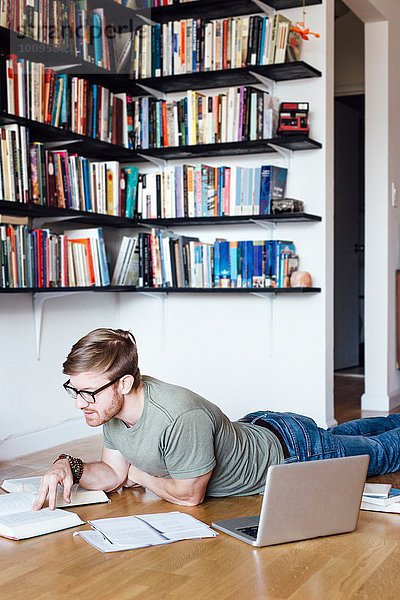 Mittlerer Erwachsener Mann  der auf dem Boden liegt und durch Bücher schaut.