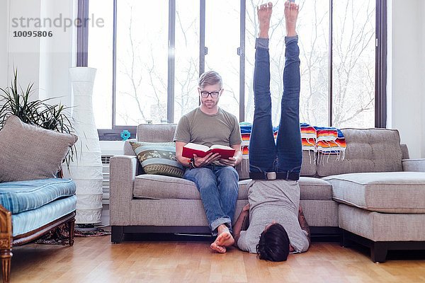 Männliches Paar zu Hause  mittlerer erwachsener Mann liest  während der Partner auf der Schulter steht.