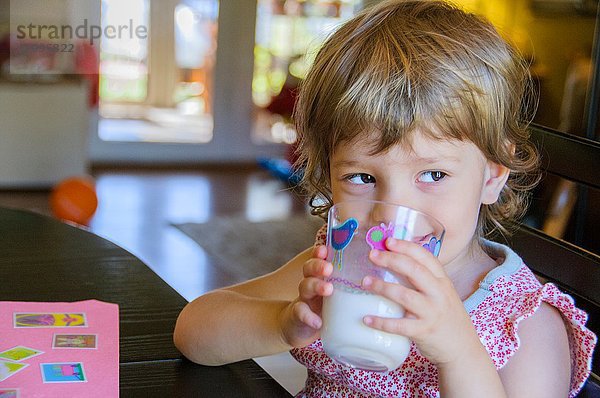 Porträt eines süßen jungen Mädchens  das am Küchentisch ein Glas Milch trinkt.