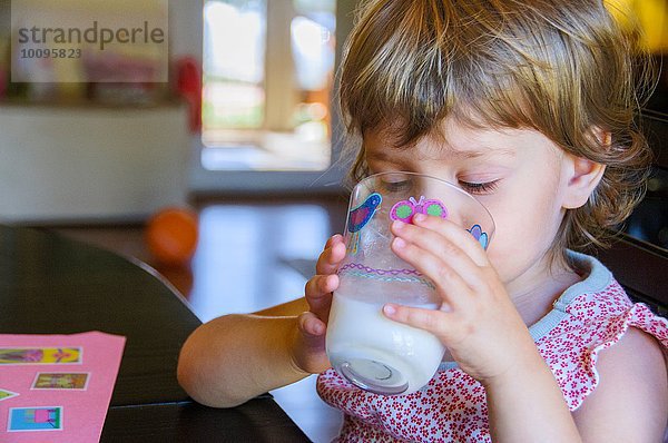 Süßes  junges Mädchen trinkt ein Glas Milch am Küchentisch.