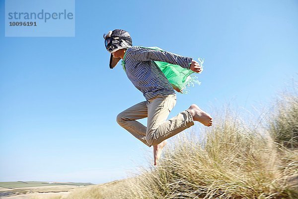 Kleiner Junge am Strand  trägt Kostüme  tut so  als würde er fliegen.