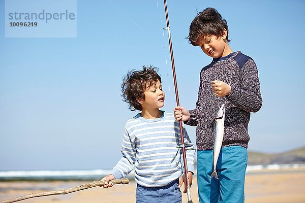 Zwei kleine Jungen stehen zusammen und halten Angel und Fisch.