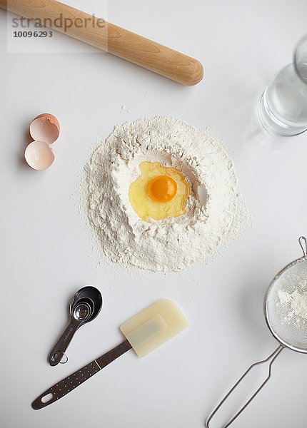 Draufsicht mit rohem Ei in der Mitte des Mehlstapels und Küchenutensilien