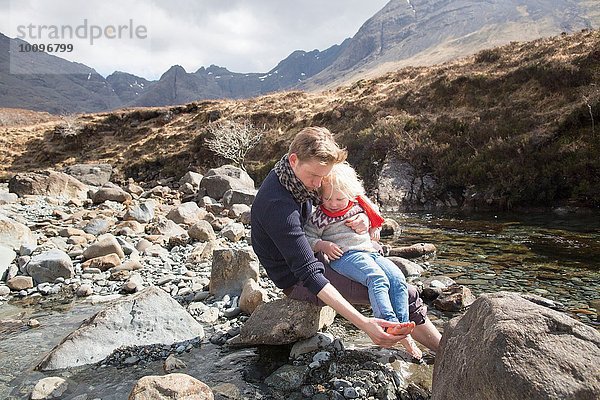 Vater und Sohn sitzen auf Felsen  Fairy Pools  Isle of Skye  Hebrides  Schottland