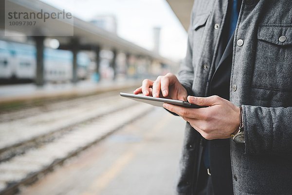 Abgeschnittenes Bild eines jungen Geschäftsmannes  der am Bahnhof die Hände eines Pendlers mit Hilfe eines digitalen Tabletts zeigt.