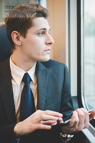 Porträt eines jungen Geschäftsmannes  der mit einem digitalen Tablett im Zug unterwegs ist.