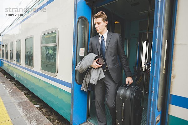 Ein junger Geschäftsmann  der den Zug mit dem Koffer verlässt.