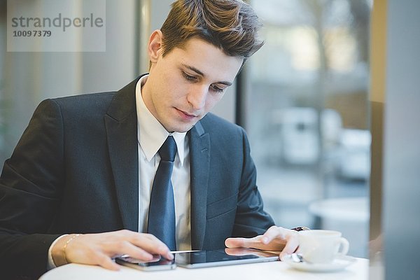 Porträt eines jungen Geschäftsmannes  der im Cafe sitzt  mit digitalem Tablett und Handy.