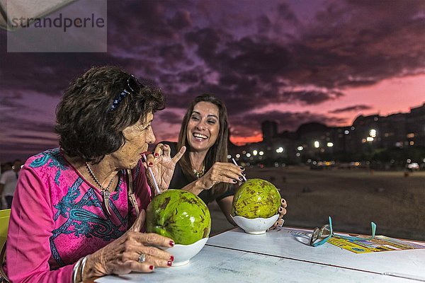 Reife Frau und Mutter trinken aus Kokosnussschalen am Strand bei Nacht  Copacabana  Rio de Janeiro  Brasilien