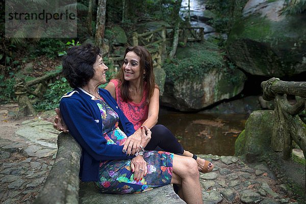 Seniorin und Tochter Händchen haltend am Waldfluss