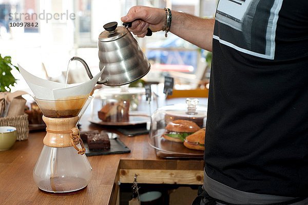 Hand des Kaffeekellners  der kochendes Wasser in die Filterkaffeekanne gießt