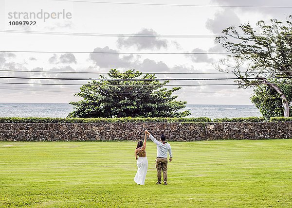 Rückansicht von Braut und Bräutigam mit erhobenen Händen im Garten der Hawaiianischen Hochzeit  Kaaawa  Oahu  Hawaii  USA