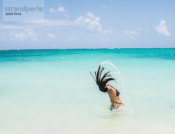 Seitenansicht einer jungen Frau  die am Lanikai Beach  Oahu  Hawaii  USA  lange nasse Haare zurück ins Meer wirft.