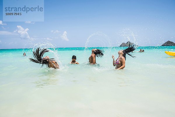 Seitenansicht von jungen Frauen  die am Lanikai Beach  Oahu  Hawaii  USA  lange nasse Haare ins Meer werfen.