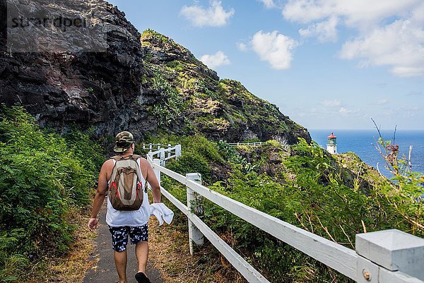 Rückansicht eines jungen männlichen Touristen  der zum Leuchtturm von Makapuuu  Oahu  Hawaii  USA geht.