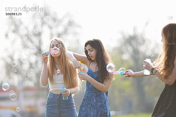 Drei Teenagermädchen beim Blasenblasen mit Blasenstab im Park