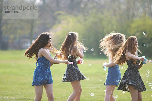 Vier Teenagermädchen beim Blasenspinnen mit Blasenstab im Park