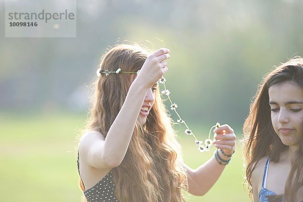 Zwei Teenager-Mädchen  die sich im Park Kopfbedeckungen anziehen.