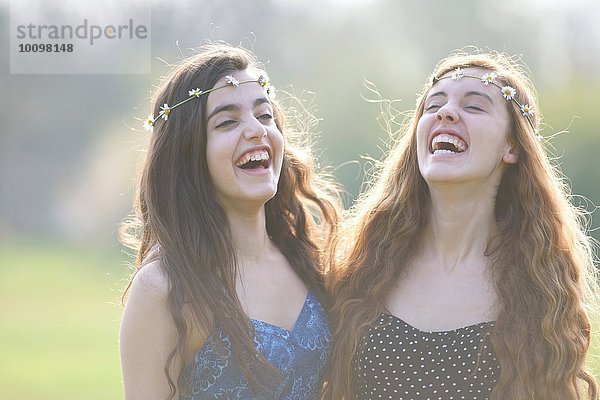 Zwei Teenager-Mädchen in Gänseblümchen-Kopfbedeckung lachend im Park