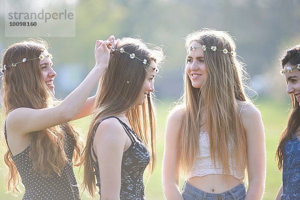 Teenagermädchen beim Anziehen und Tragen von Daisy Chain Headdresses im Park