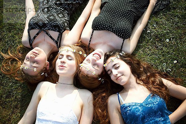 Vier Teenagermädchen in Gänseblümchen-Kopfbedeckungen auf Parkgras liegend