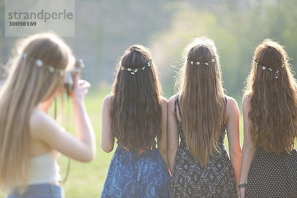 Rückansicht eines Teenagermädchens  das Freunde in Gänseblümchen-Kopfbedeckungen im Park fotografiert.