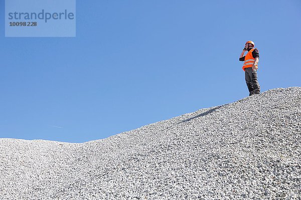 Steinbrucharbeiter beim Chatten auf dem Smartphone vom Steinbruchkieshügel aus