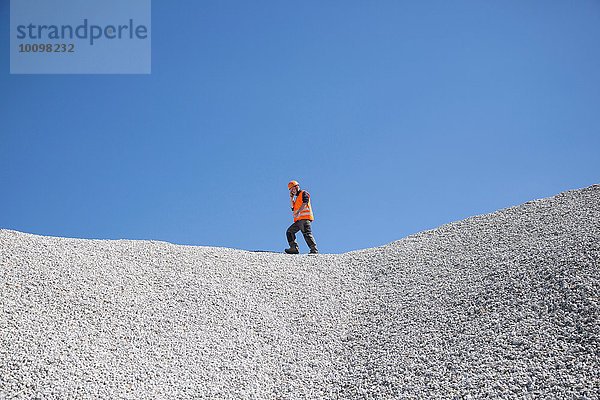 Steinbrucharbeiter beim Chatten auf dem Smartphone auf dem Steinbruchschotterhügel