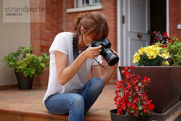 Mittlere erwachsene Frau  die im Freien sitzt und Blumentöpfe fotografiert.