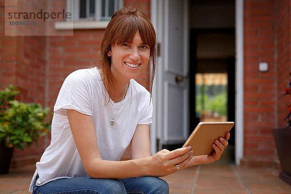 Mittlere erwachsene Frau  die im Freien sitzt und ein digitales Tablett hält.