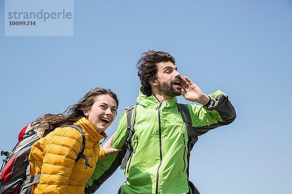 Wanderpaar gegen blauen Himmel lachend und schreiend