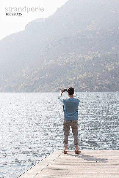 Rückansicht des jungen Mannes beim Fotografieren vom Pier  Mergozzo-See  Verbania  Piemonte  Italien