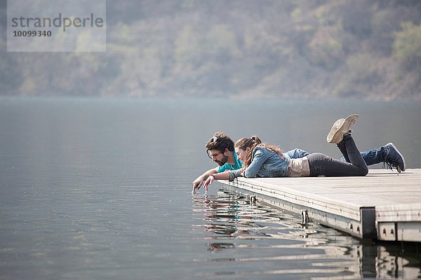 Junges Paar auf dem Pier liegend  tauchende Finger im Mergozzo-See  Verbania  Piemonte  Italien